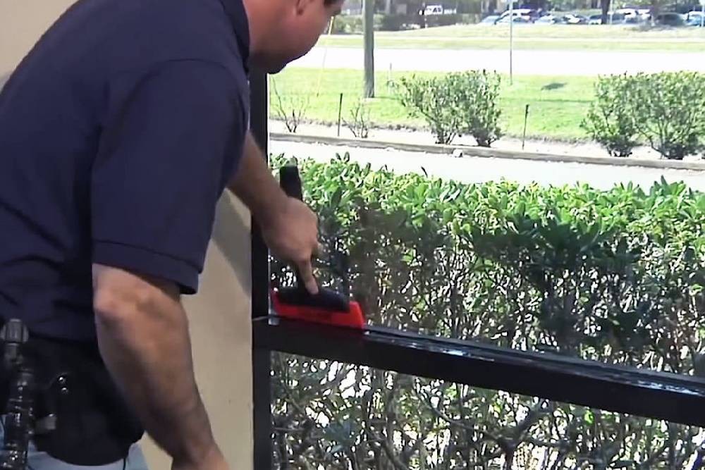 A man in a blue shirt installs a transparent Madico window film with a special tool